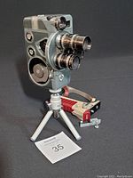 Front and side view of the Arco 8 movie camera mounted on a small tripod, showing the dual lenses and winding mechanism.