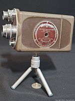 Side view of 1940s Bell & Howell Auto Master 16mm movie camera mounted on mini tripod, showing textured brown body and three lenses.