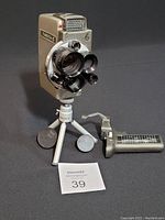 Front and side view of the Yashica C movie camera mounted on a small tripod with original handle placed beside it.