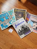 Thirteen Goldmine music magazines arranged on floor showing some front covers, artwork and artists.