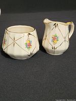 Front view of a creamer and sugar bowl showing floral and gold diamond design with scalloped edges