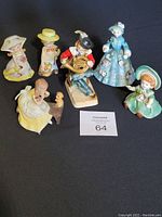 Overview of all six vintage porcelain figurines arranged on a dark surface, showing variety and condition