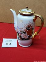 Side view of the vintage porcelain tea pot showing floral hand painted design, gold handle, and scenic lid painting.
