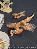 Two flying pheasant figurines shown, one larger and one smaller, with detailed textured feathers and natural coloring, placed on a black background.