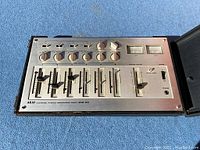 Full view of the Akai MM-62 stereo microphone mixer showing the layout of faders, knobs, meters, and power switch in the protective case.