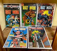 Five Batman comic books from the 1980s displayed upright and stacked, showing colorful cover art with Batman and other characters in action poses.