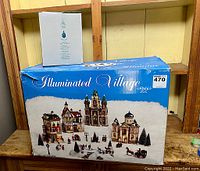 Original box of 26-piece Illuminated Village Christmas ceramic set displayed on wooden surface, showing set branding and packaging.