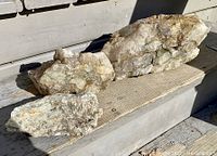 Photo showing three large quartz rocks with rusty seams arranged on wooden steps in sunlight