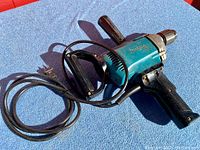 Full view of Makita electric drill driver laid on a blue surface, showing cord and handle.