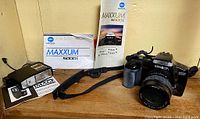 Minolta Maxxum 5000i camera with zoom lens, manuals, flash unit, and strap displayed on wood surface.