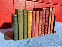 Group view of eleven smaller antique decorative books in various colors and bindings, standing upright with bookends.