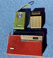 Photo showing three vintage transistor radios on blue carpet: green Bradford radio, black and cream radio, and red Sony radio