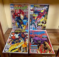 Four Spider-Man comic books placed on a wooden surface, showing front covers with characters such as Spider-Man, Ghost Rider, and Swarm.