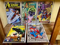 Photo showing five bagged and boarded Action Comics comic books from the 1980s and early 1990s featuring Superman and related characters with vibrant cover art.