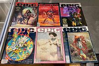 Six vintage Epic Illustrated magazines from 1981-1984 with various fantasy and sci-fi cover art showing characters such as a knight on horseback, cosmic warriors, and surreal fantasy figures, laid out flat on a table.