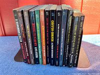 Photo showing the spines of 14 Alfred Hitchcock murder mystery paperbacks lined up side by side