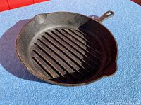 Photo showing angled view of vintage cast iron grill pan with ridged grill surface, two pouring spouts, and handle.