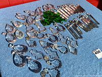 All chandelier parts laid out on blue fabric surface, showing variety of crystal shapes and colors including clear and green crystals.