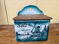 Front view of the teal and white ceramic salt box showing Dutch windmill and 'Salz' lettering with a hinged wooden lid closed.
