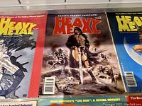 Close-up view of three Heavy Metal magazine covers featuring illustrated fantasy and sci-fi characters in detailed color.