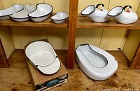 Shelved vintage white enamelware medical items including emesis basins, urinals, and bed pan. Bed pan branded 'Jones' in mint condition inside a box.