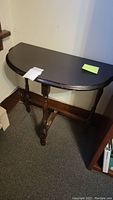 Photo of the antique three-legged semi-circular console table from an angled front view showing the top and legs.
