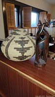 Photo of the woven basket with lid and the wooden giraffe statuette side by side on a wooden surface.