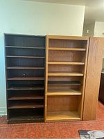 Photo showing two tall wooden bookshelves side by side, one black with seven shelves, one natural wood finish with six shelves and a darker shelf in the middle.