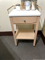 Portable metal cabinet with pinkish-beige finish, white top, one drawer opened showing interior, and caster wheels, appearing lightly used.