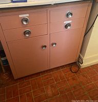 Front view of the pink metal cabinet showing multiple drawers and cabinet doors with round silver handles.