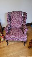 Front view of the floral wingback chair, showing upholstery and wooden legs.
