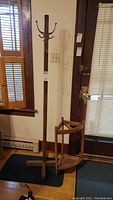 Full view of tall wooden coat rack with multiple hooks near door and window.