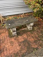 Concrete outdoor bench placed on brick patio against house siding, showing full bench with seat and legs attached.