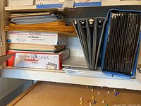 Shelf with stacked catalog envelopes, black 3-ring binders, and accordion filing case.
