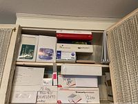 Shelves with multiple boxes and binders including labeled boxes of security envelopes and billing envelopes, phone message pads, and thank you cards visible.