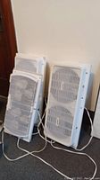 Two White Westinghouse twin window fans stacked against wall showing front grills and power cords.