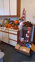 Wide view of counter with Halloween, fall, and Christmas decorations including pumpkin bucket, ghost figure, wreath, and assorted small items in boxes.