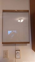 Full front view of the light box mounted on a wall showing rectangular shape, textured brown frame, frosted white surface, and attached dimmer switch below.