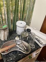 A countertop with vintage medical supplies including white enamel lidded containers, metal kidney tray with wooden pestle, various glass jars and containers, and metal and glass medical instruments.