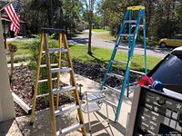 Green Bull 6-foot fiberglass and aluminum step ladder and Werner 8-foot fiberglass and aluminum step ladder standing outside on pavement.