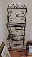 Full view of the wrought iron bakers rack showing the three shelves and decorative scrollwork.