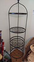 Front angled view of the metal bakers rack showing spiral shelves and wine rack section near bottom with some rust.