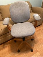 Front view of bentwood office chair with light grey fabric backrest, seat and arm pads against a brown couch background.