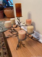 Photo of metal candelabra with six pillar candles on wooden floor against wall.