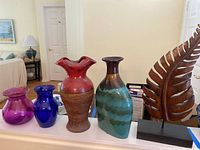 All four vases alongside the wooden leaf sculpture displayed on a white surface in an interior setting.