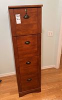Front view of tall wooden filing cabinet with four drawers, showing wood finish and black metal handles.