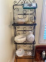 Overview of six main items displayed on black metal rack including desk lamp on top, stoneware vase and planter in middle, and smaller ceramics and casserole dish at bottom