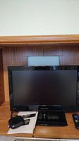 Front view of the 19-inch Proscan LED television on a wooden shelf, showing the screen, remote, power adapter, and user manual placed next to it.