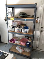 Front view of five-shelf metal shelving unit containing baskets, watering can, ceramic planters, and plastic containers.