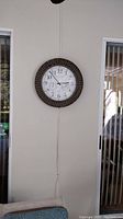 Full view of the outdoor clock mounted on a white wall near windows and a couch.